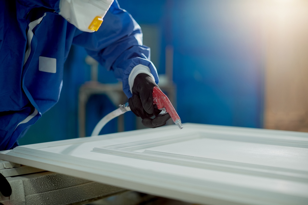 closeup worker spraying paint processed wood production facility